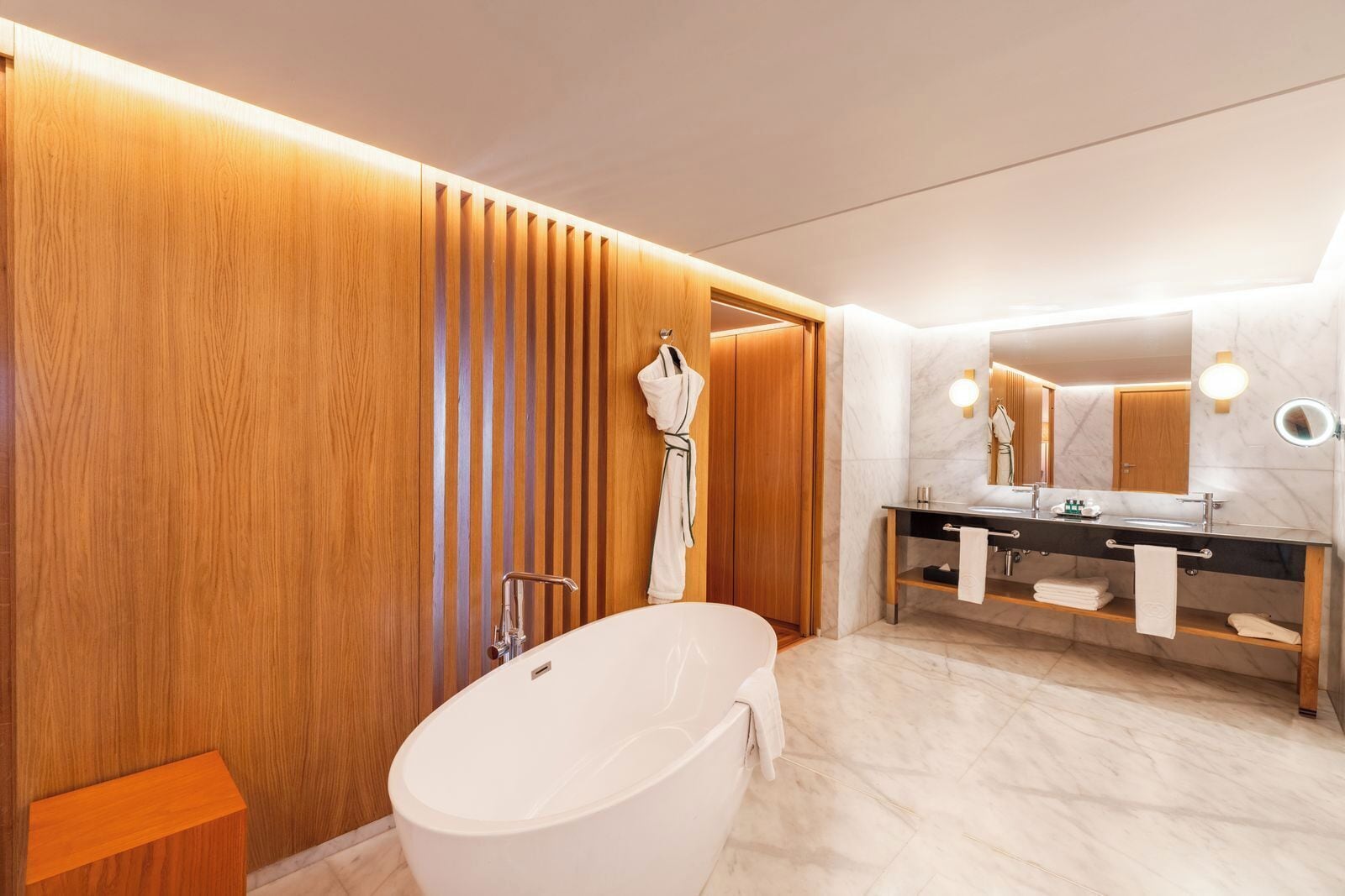 A modern bathroom with a freestanding bathtub, a vanity with a mirror, and wooden paneling on the walls.