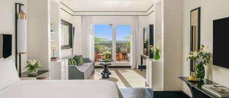 A hotel room with a large bed, a sofa, a TV, a balcony with a view, and a dining area.