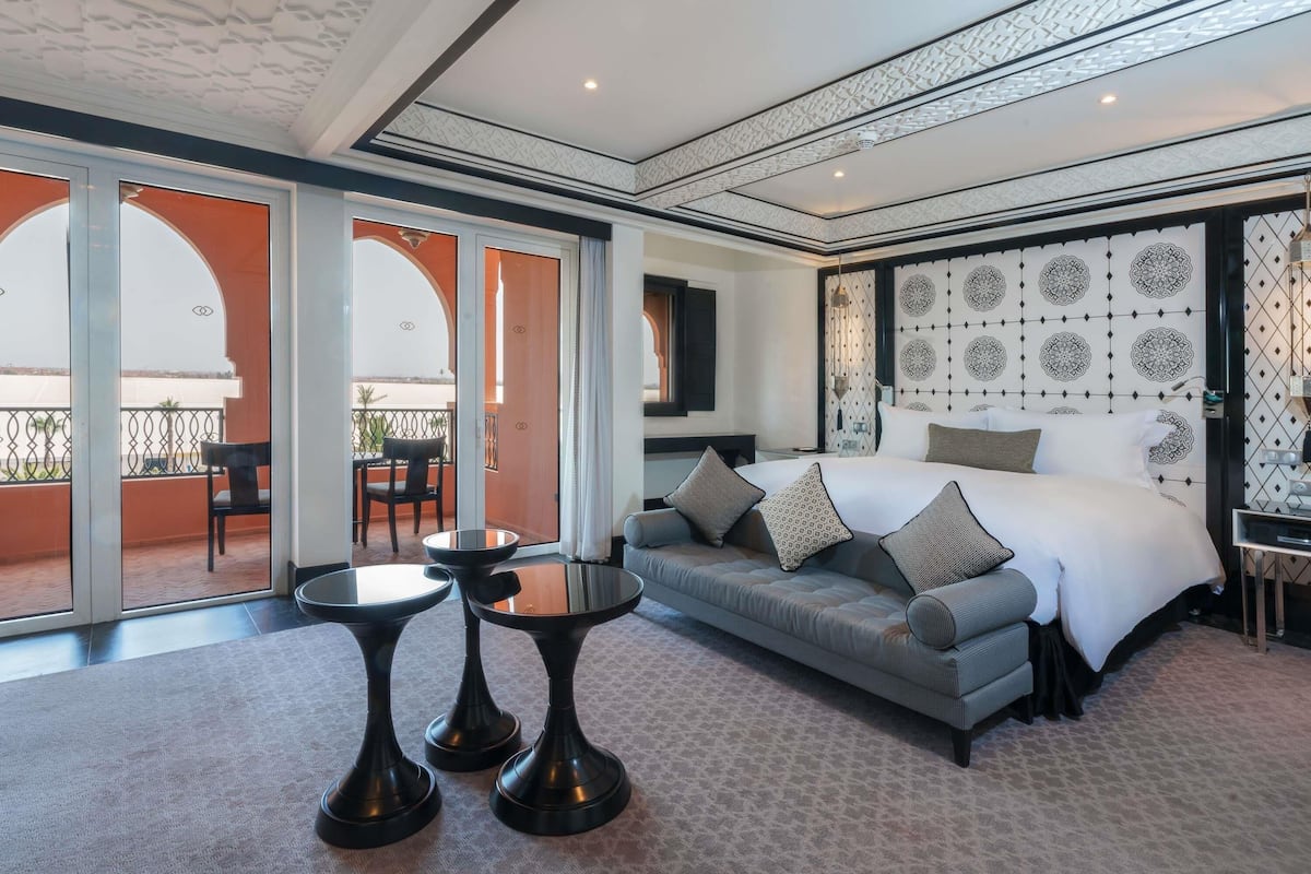 A hotel room with a large bed, a sofa, two small tables, and a balcony with a view.