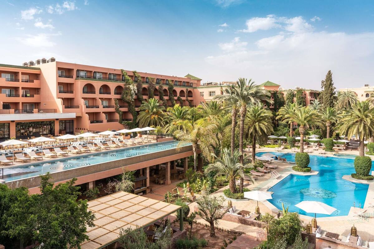 Un hotel con varias piscinas, palmeras y zonas de estar al aire libre.