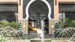 Un edificio con una amplia entrada en arco, una fuente en primer plano y baldosas decorativas en las paredes.