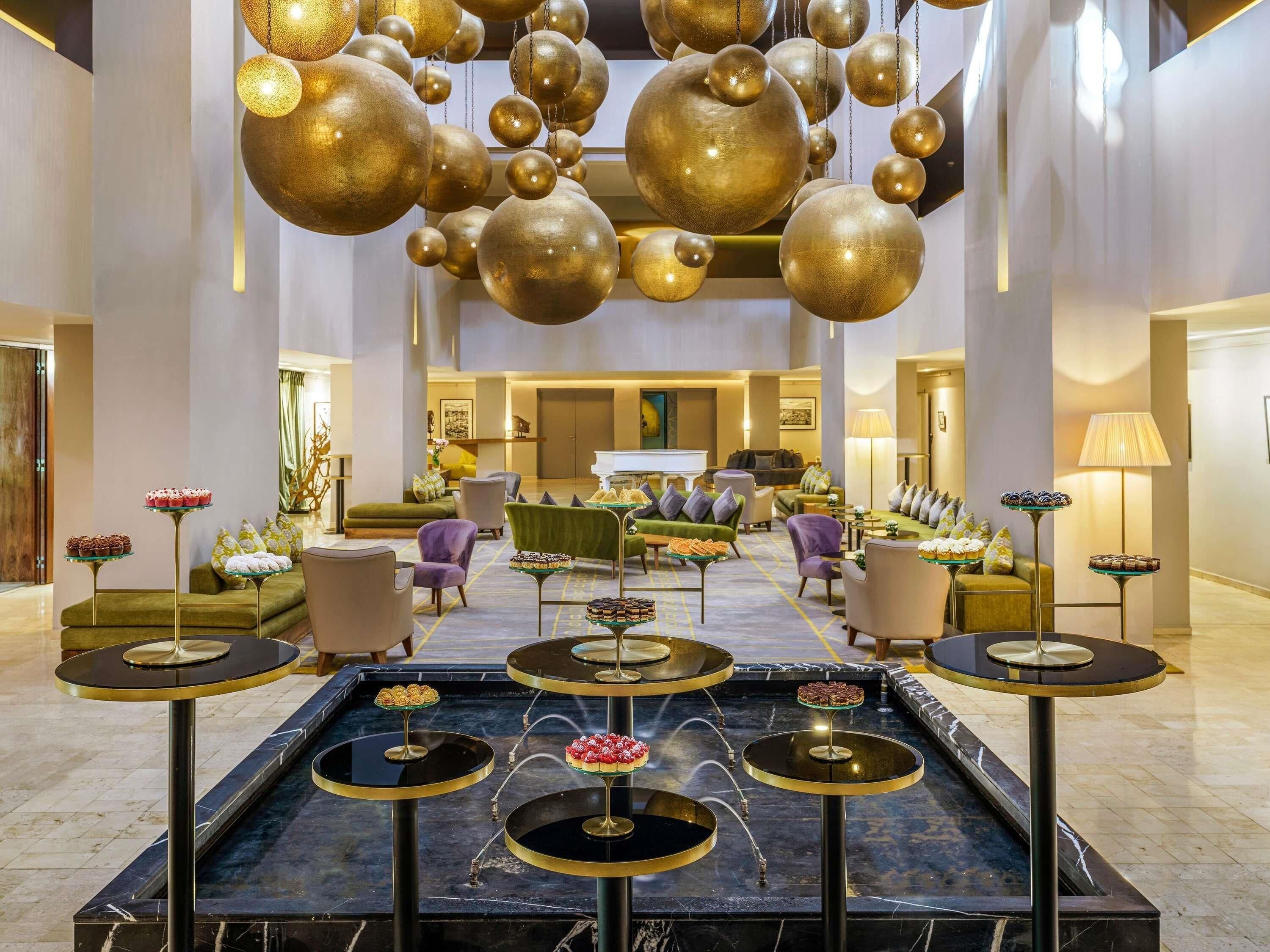 A spacious lobby with a central water feature, seating areas, and a grand chandelier.