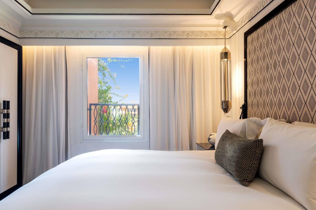 A hotel room with a large bed, a window with curtains, a balcony, and a patterned wall.
