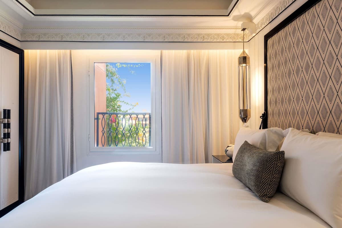 A hotel room with a large bed, a window with curtains, a balcony, and a patterned wall.