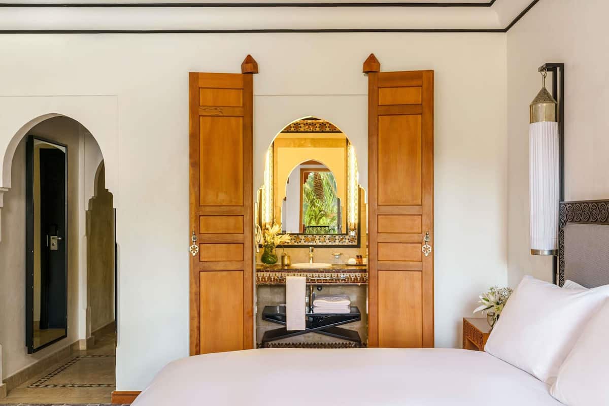 A hotel room with a large bed, a bathroom with a mirror, and a hallway leading to another room.