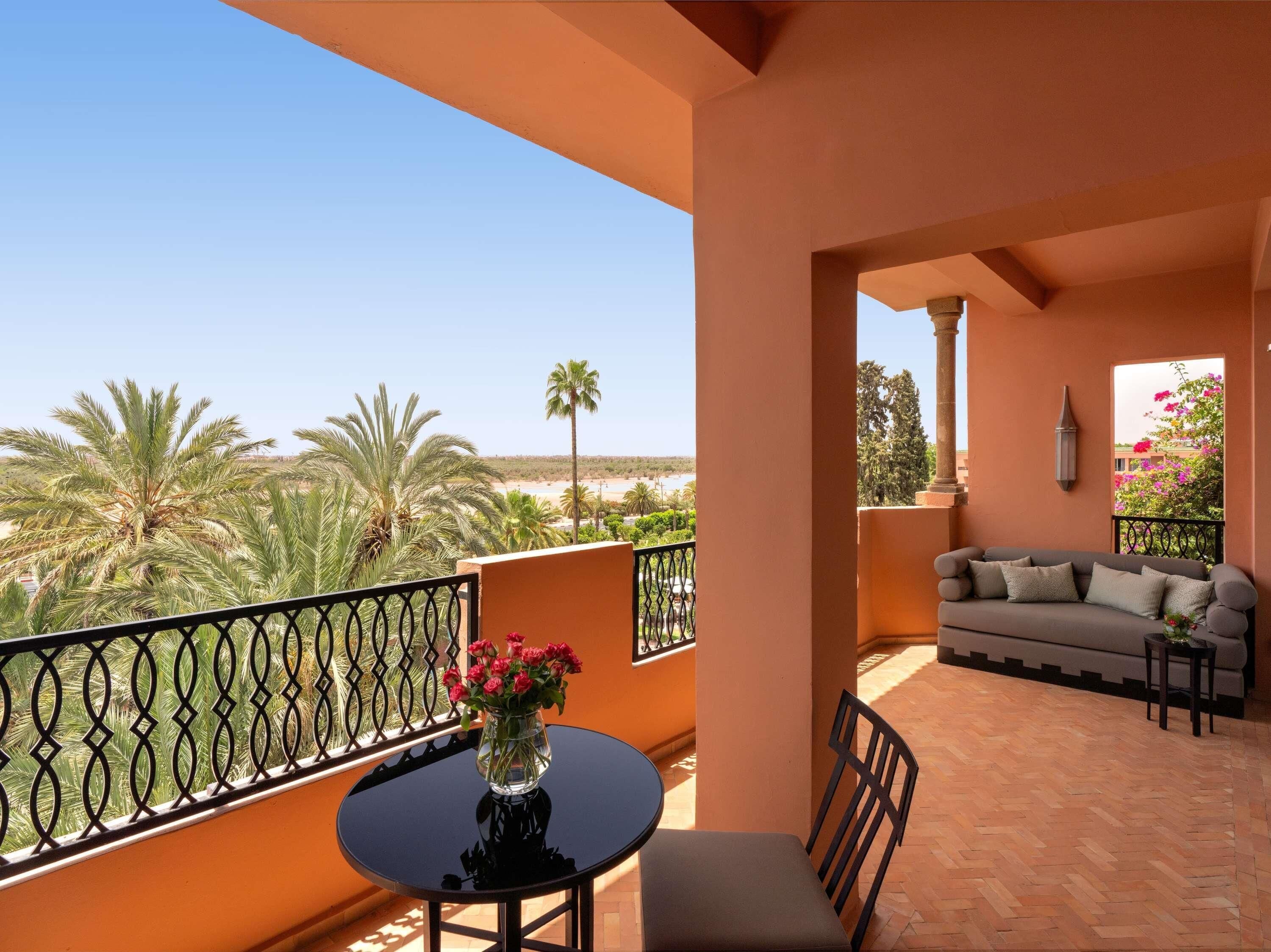 A balcony with a table and chairs, a sofa, and a view of palm trees and a beach.