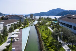 A modern hotel with a swimming pool, lush greenery, and a view of the sea and mountains.