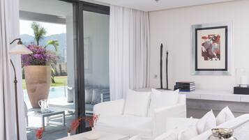 Un salón moderno con un sofá blanco, una mesa de centro y un amplio ventanal con vistas a una piscina y vegetación.