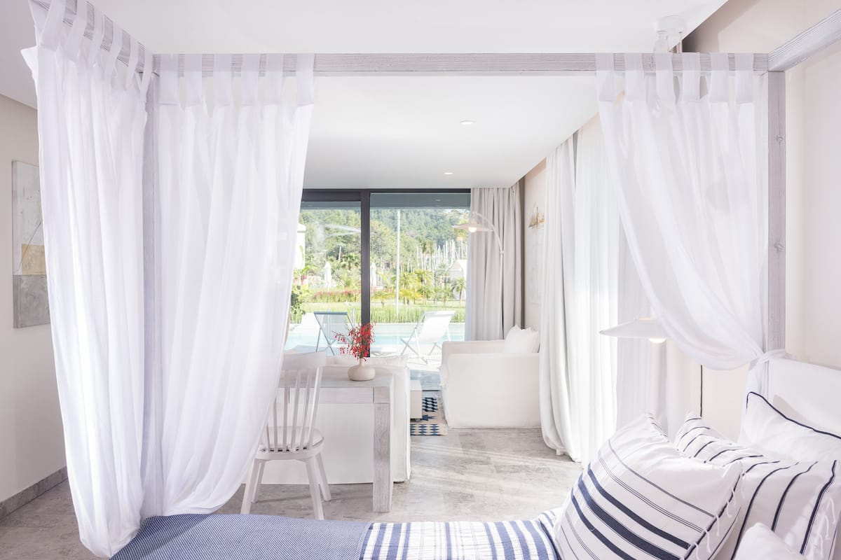 Ein modernes Hotelzimmer mit Bett, Schreibtisch und Blick auf Pool und Grünfläche.