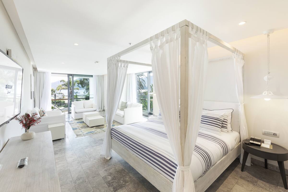 Ein modernes Schlafzimmer mit Himmelbett, einer Sitzecke mit Sofa und Sesseln sowie Blick ins Freie.
