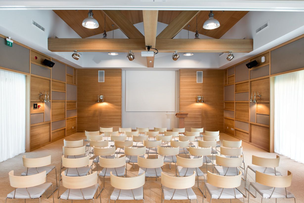 Un salón de conferencias con hileras de sillas, paneles de madera y luces en el techo.