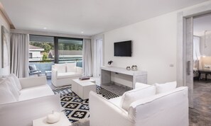 Una sala de estar moderna con un sofá blanco, una mesa de centro y un televisor montado en la pared. Hay un balcón con vistas al exterior.