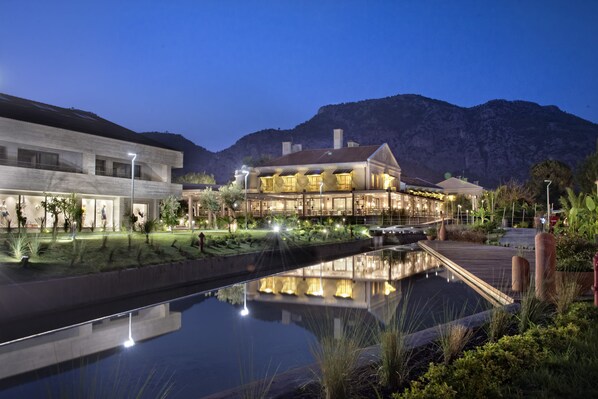 Un hotel moderno con una piscina reflectante, una terraza de madera y montañas al fondo.