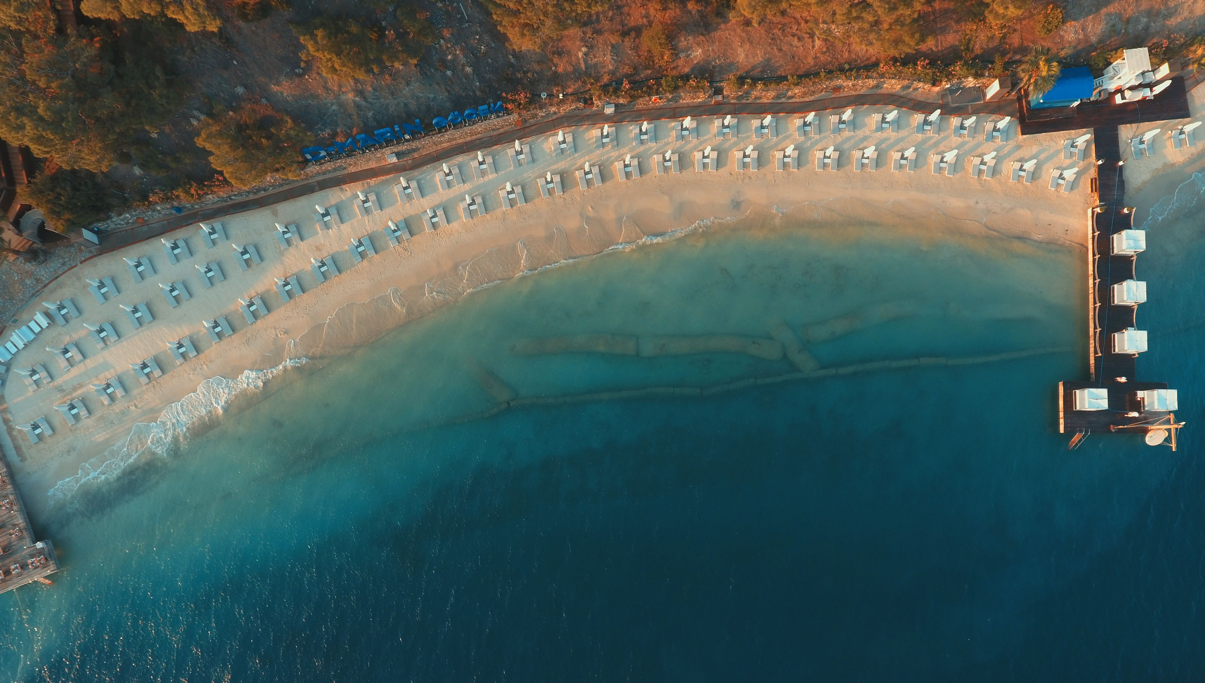 An aerial view of a beach with rows of sun loungers and a swimming pool.