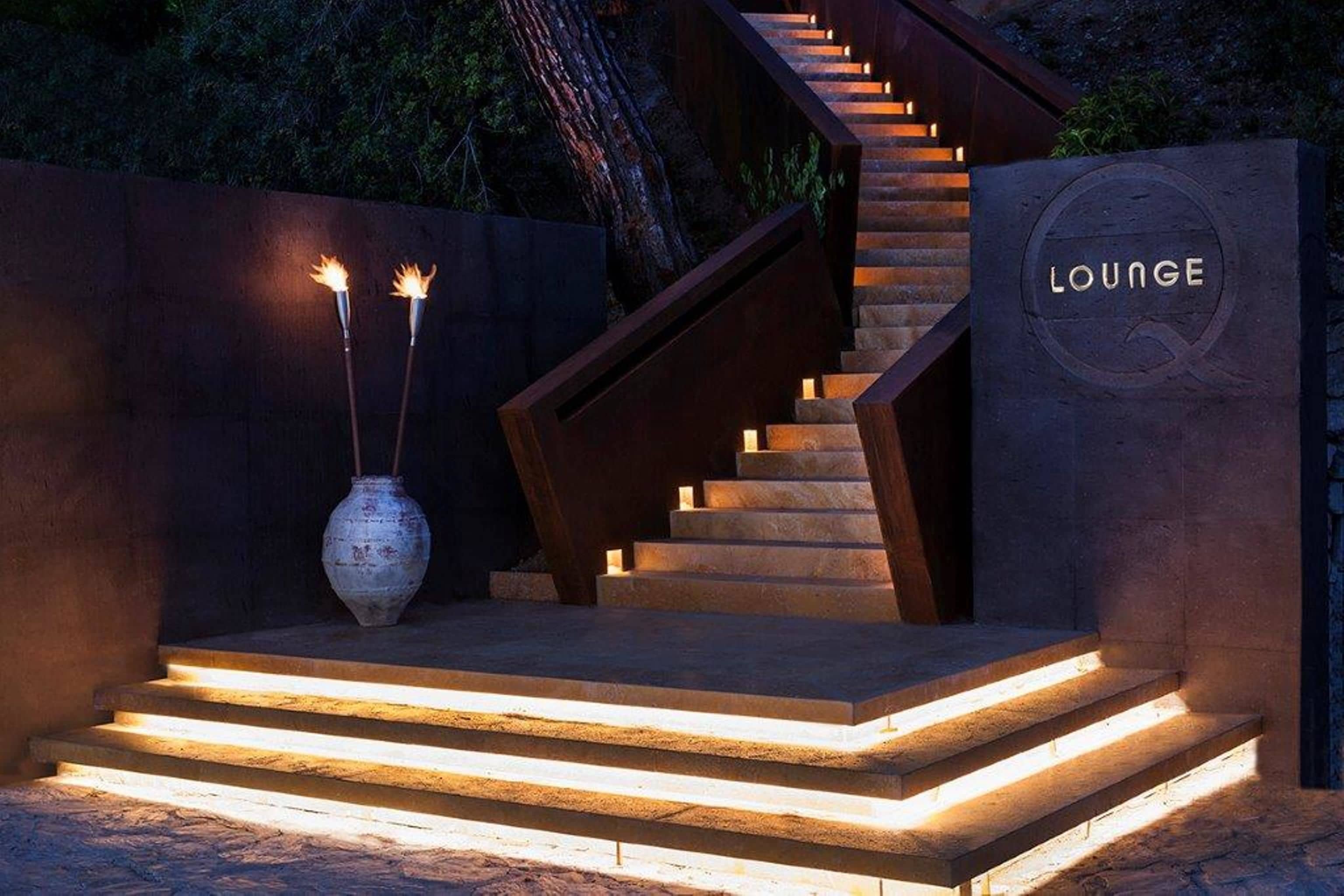 Una escalera conduce a un área de estar con una pared de piedra y un letrero que dice "LOUNGE".
