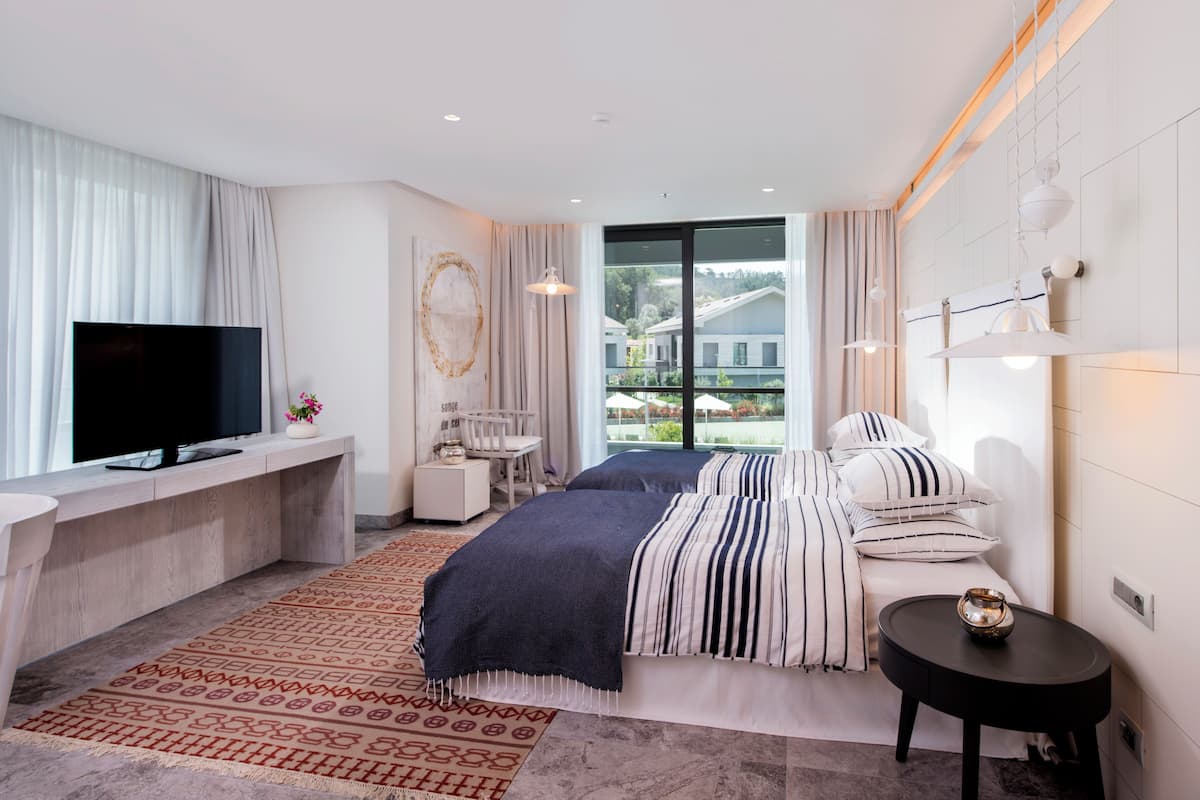 Ein modernes Schlafzimmer mit einem großen Bett, einem Fernseher, einem Schreibtisch und Blick ins Freie.