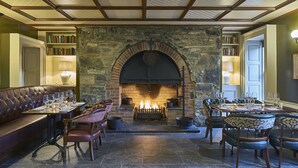 Un rincón comedor acogedor con chimenea de piedra, asientos de cuero y una estantería llena de libros.