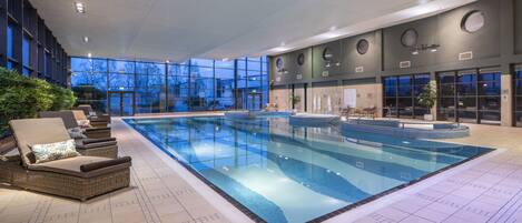 An indoor swimming pool with lounge chairs, a hot tub, and a view of the outside.