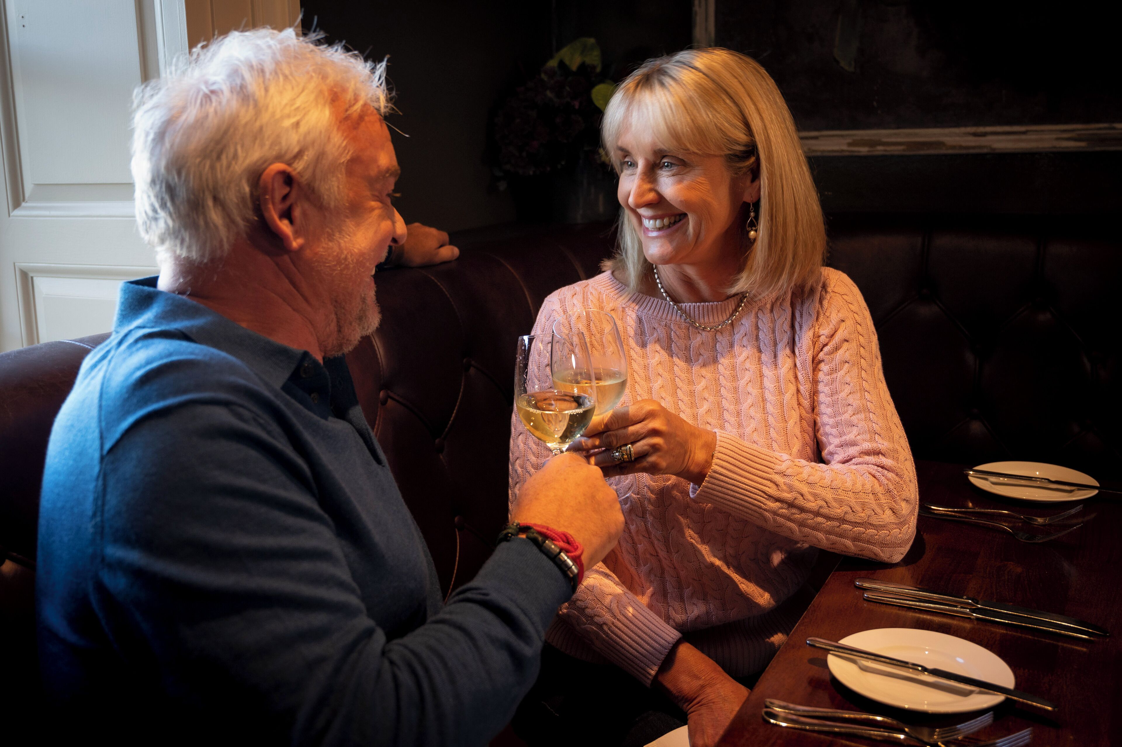Two people sitting at a table with a glass of wine, a plate, and cutlery.