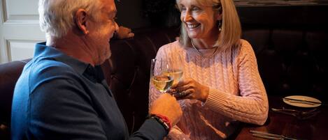 Two people sitting at a table with a glass of wine, a plate, and cutlery.