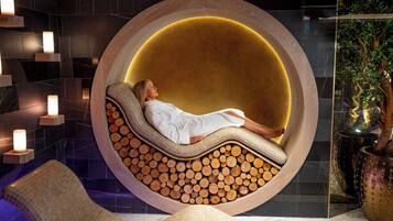 A spa room with a circular wooden bench, a person relaxing, and a wall with candles.