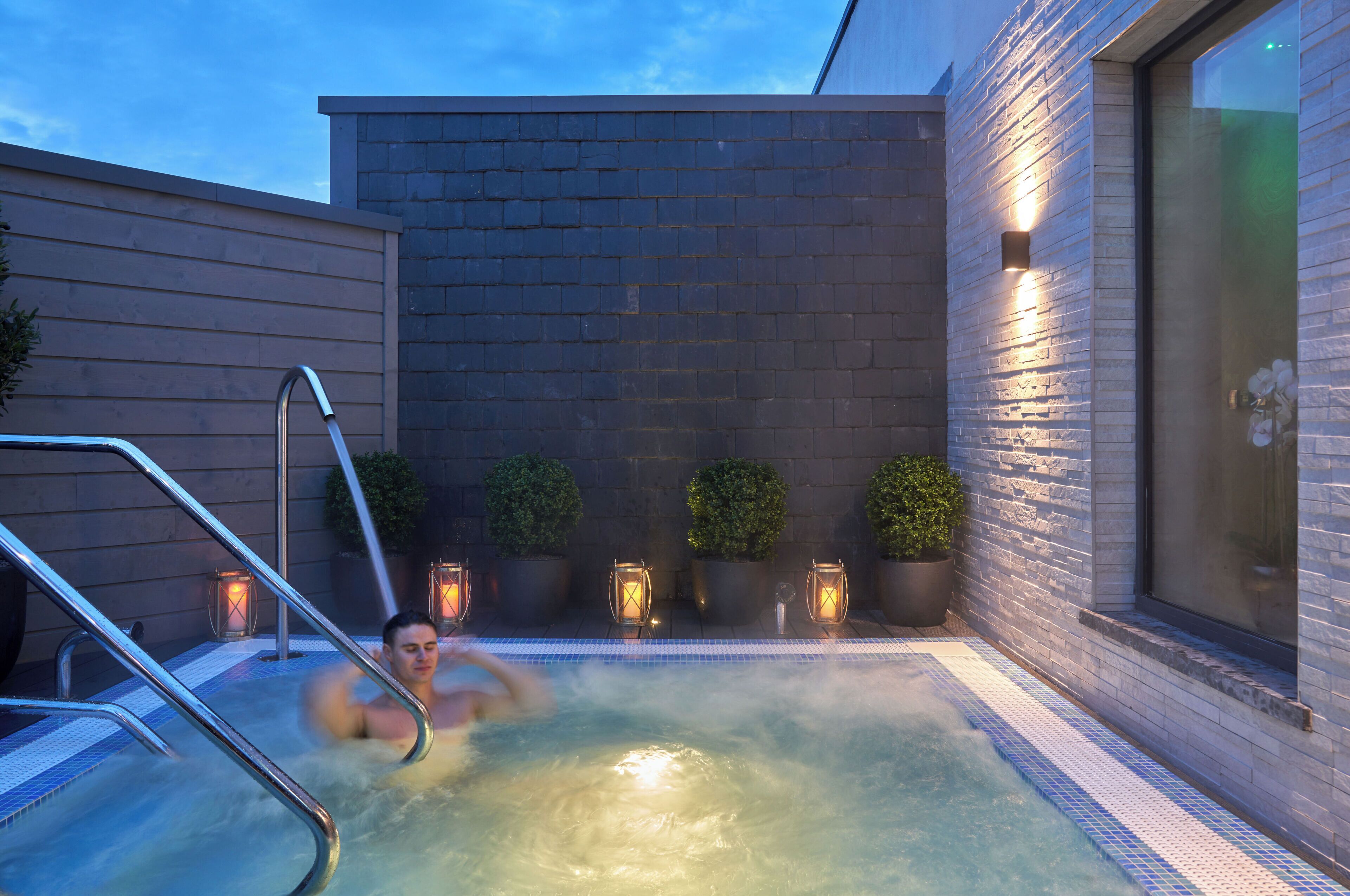 A hot tub area with a brick wall, potted plants, and a glass door.