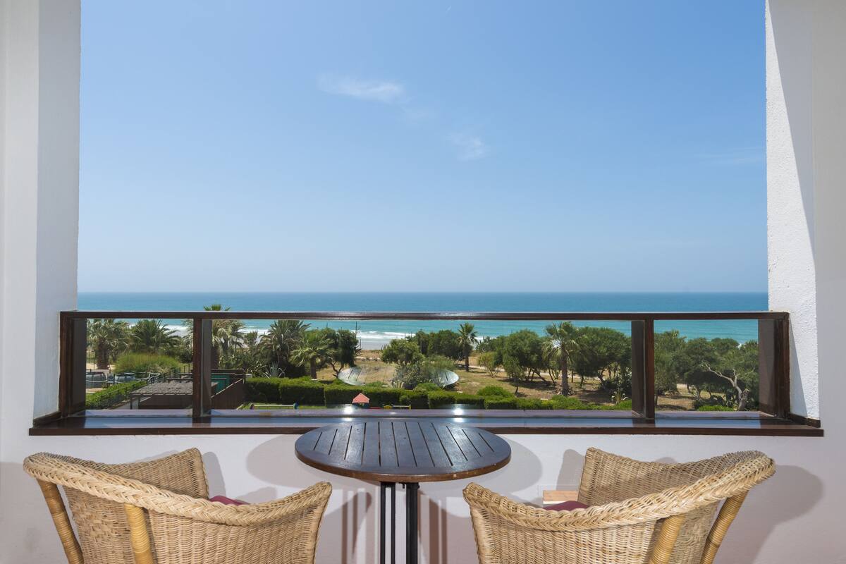 A balcony with a view of the ocean, a round table, and wicker chairs.