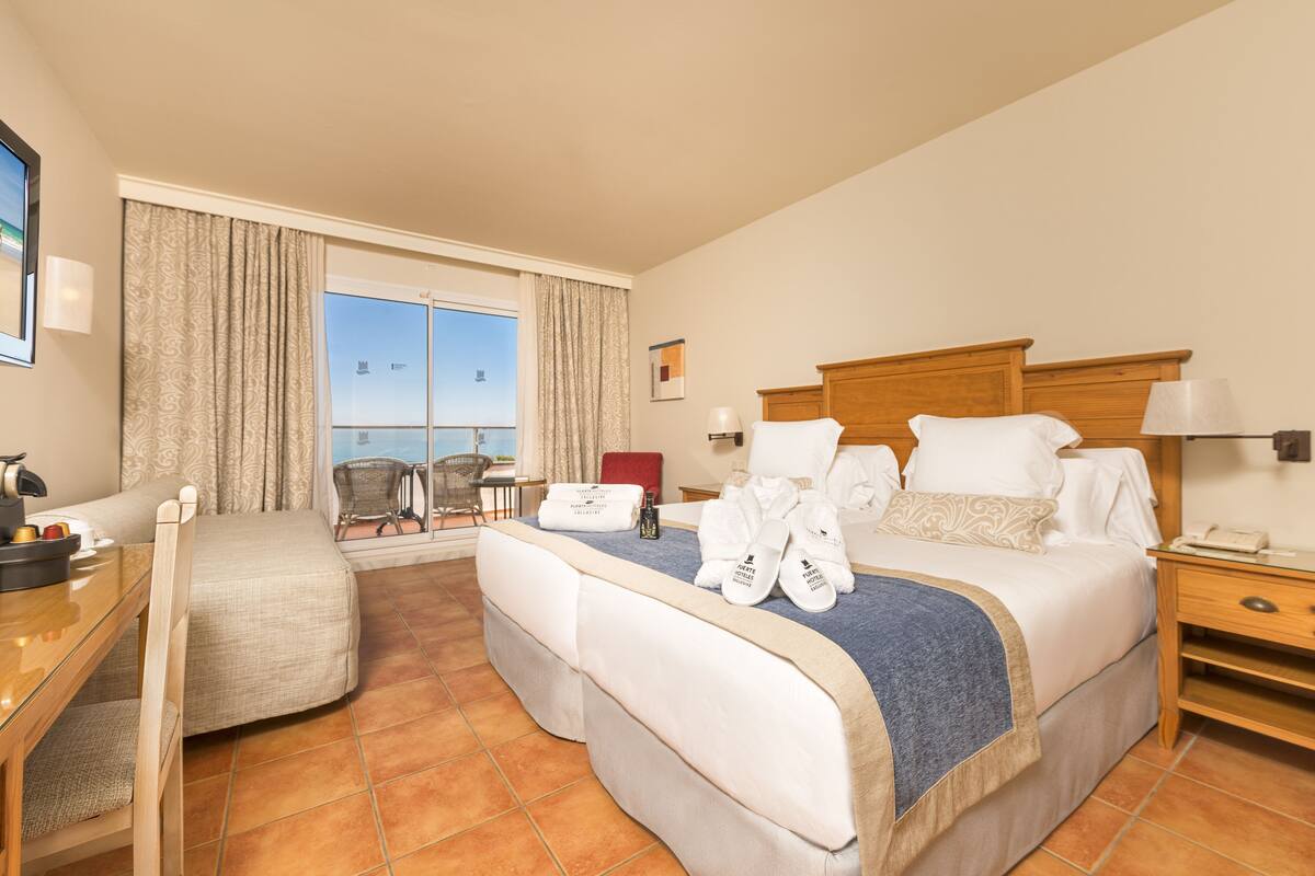 A hotel room with two beds, a desk, a chair, a small table, and a window with curtains.
