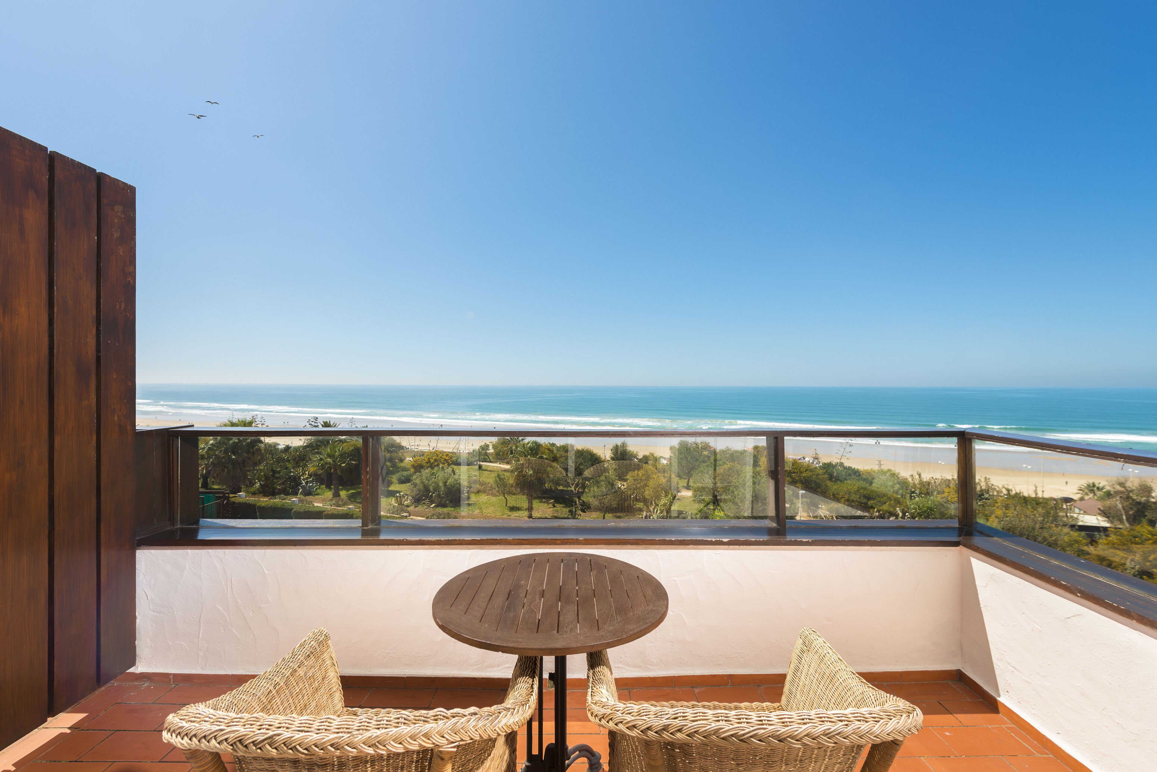 A balcony with a view of the ocean, a round table, and two wicker chairs.