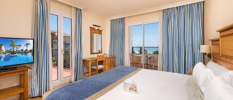 Habitación de hotel con una cama grande, un escritorio, televisión y balcón con vista al océano.