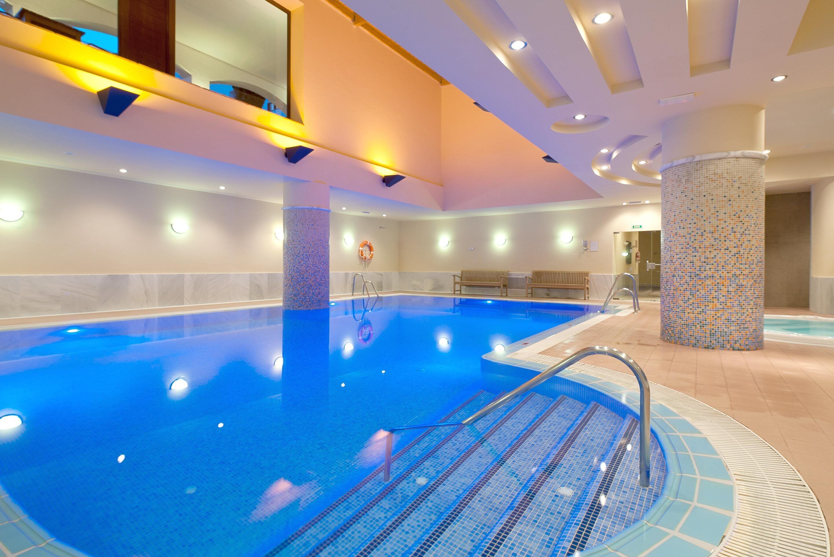 A large indoor swimming pool with a tiled deck area, a changing room, and a reception desk.