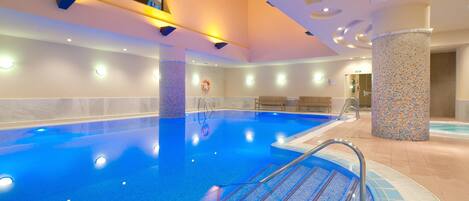 A large indoor swimming pool with a tiled deck area, a changing room, and a reception desk.