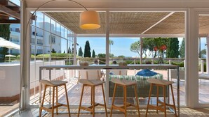 A balcony with wicker bar stools, a table, and a view of the sea and buildings. - Hotel Fuerte Conil-Resort (Conil de la Frontera)