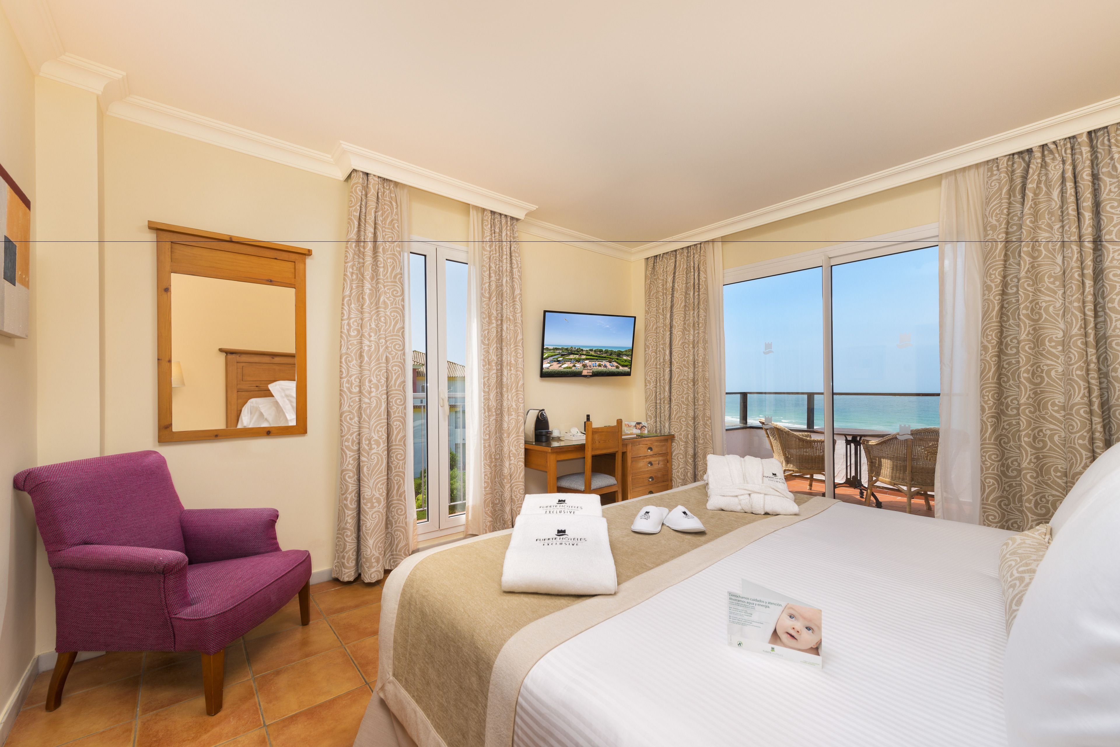 Una habitación de hotel con cama, escritorio, silla, televisión y vista al océano.