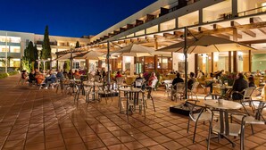 An outdoor dining area with multiple tables and chairs, surrounded by a modern building with balconies. - Hotel Fuerte Conil-Resort (Conil de la Frontera)