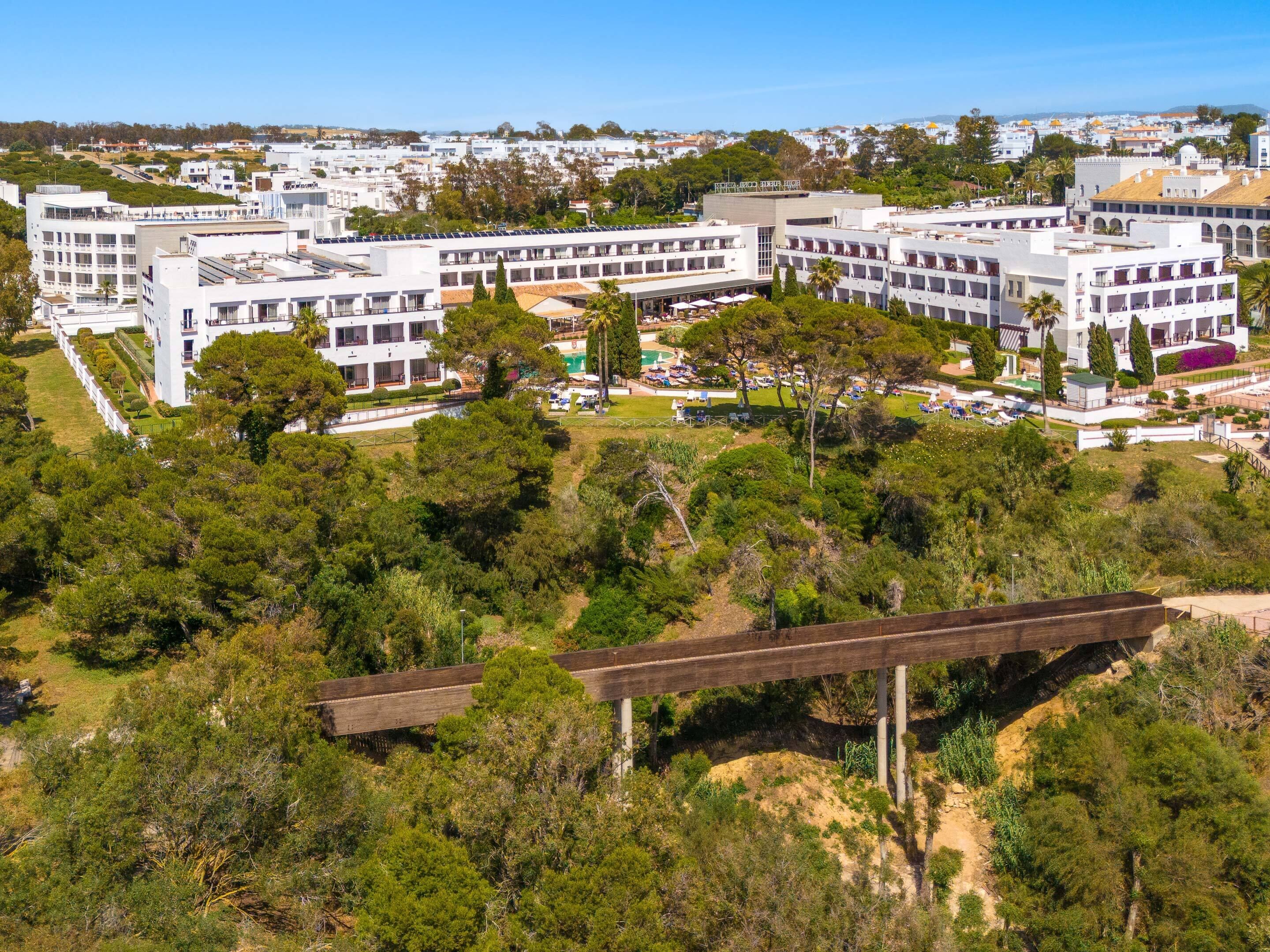 A modern hotel complex with multiple buildings, a central courtyard with seating, and surrounding greenery.