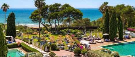A resort pool area with sun loungers, umbrellas, and a view of the sea.