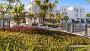 A modern hotel with a white facade, palm trees, and a landscaped garden with colorful flowers. - Hotel Fuerte Conil-Resort (Conil de la Frontera)