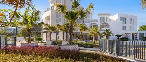 Un hôtel moderne à la façade blanche, agrémenté de palmiers et doté d’un jardin paysager aux fleurs multicolores.