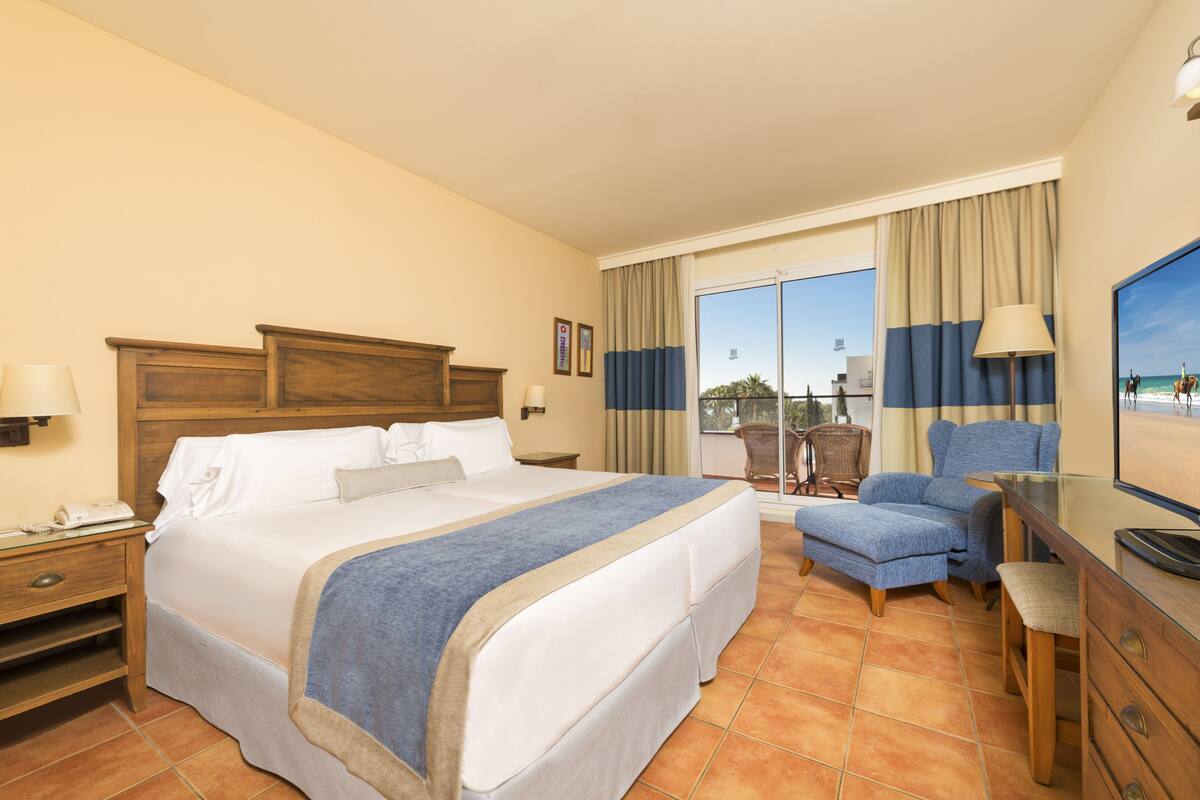 A hotel room with a large bed, a desk, a chair, a TV, and a balcony with a view.