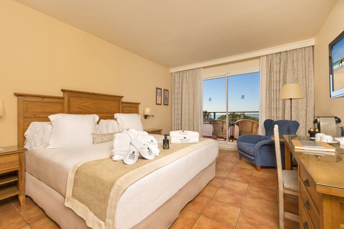 A hotel room with a large bed, a desk, a chair, and a view of the outdoors.