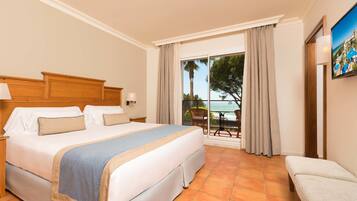 Habitación de hotel con una cama grande, una mesita, una silla y un balcón con vistas al mar.