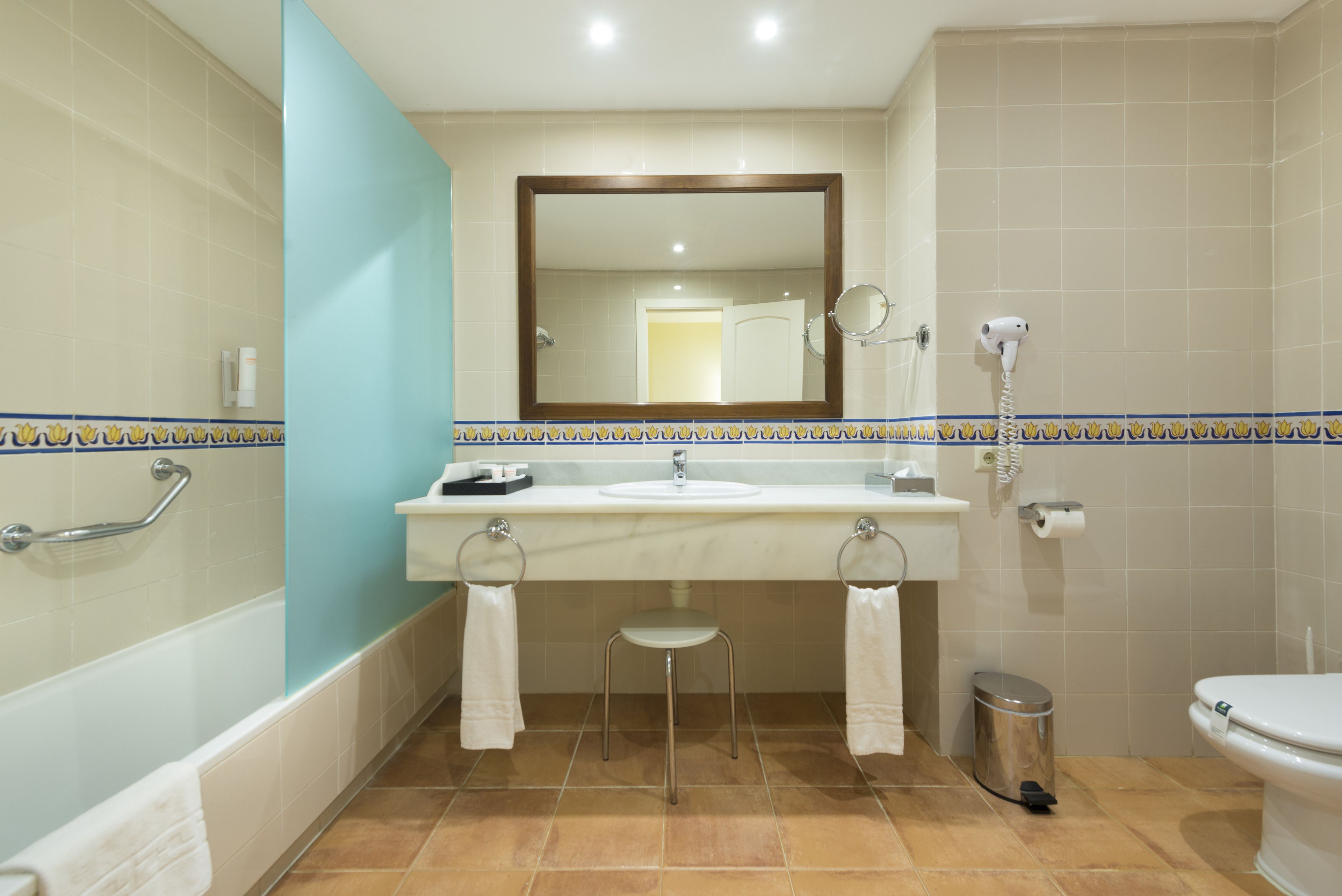 A bathroom with a bathtub, a sink with a mirror above it, a toilet, and a trash can.