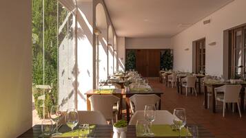 Un restaurante con varias mesas, sillas y vistas a zonas verdes a través de amplios ventanales.