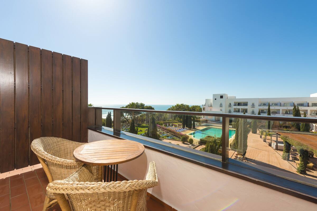 A balcony with wicker furniture and a view of a swimming pool and buildings.