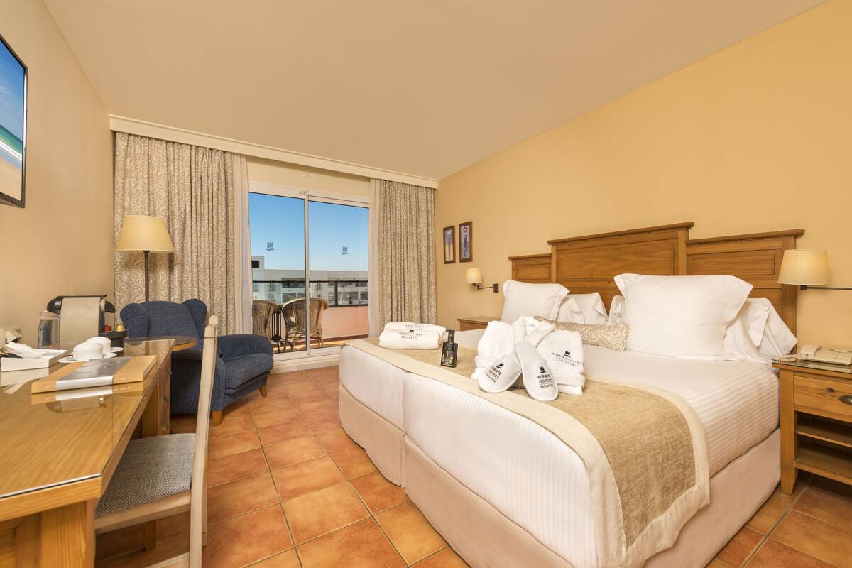 A hotel room with a bed, a desk, a chair, and a view of the city.