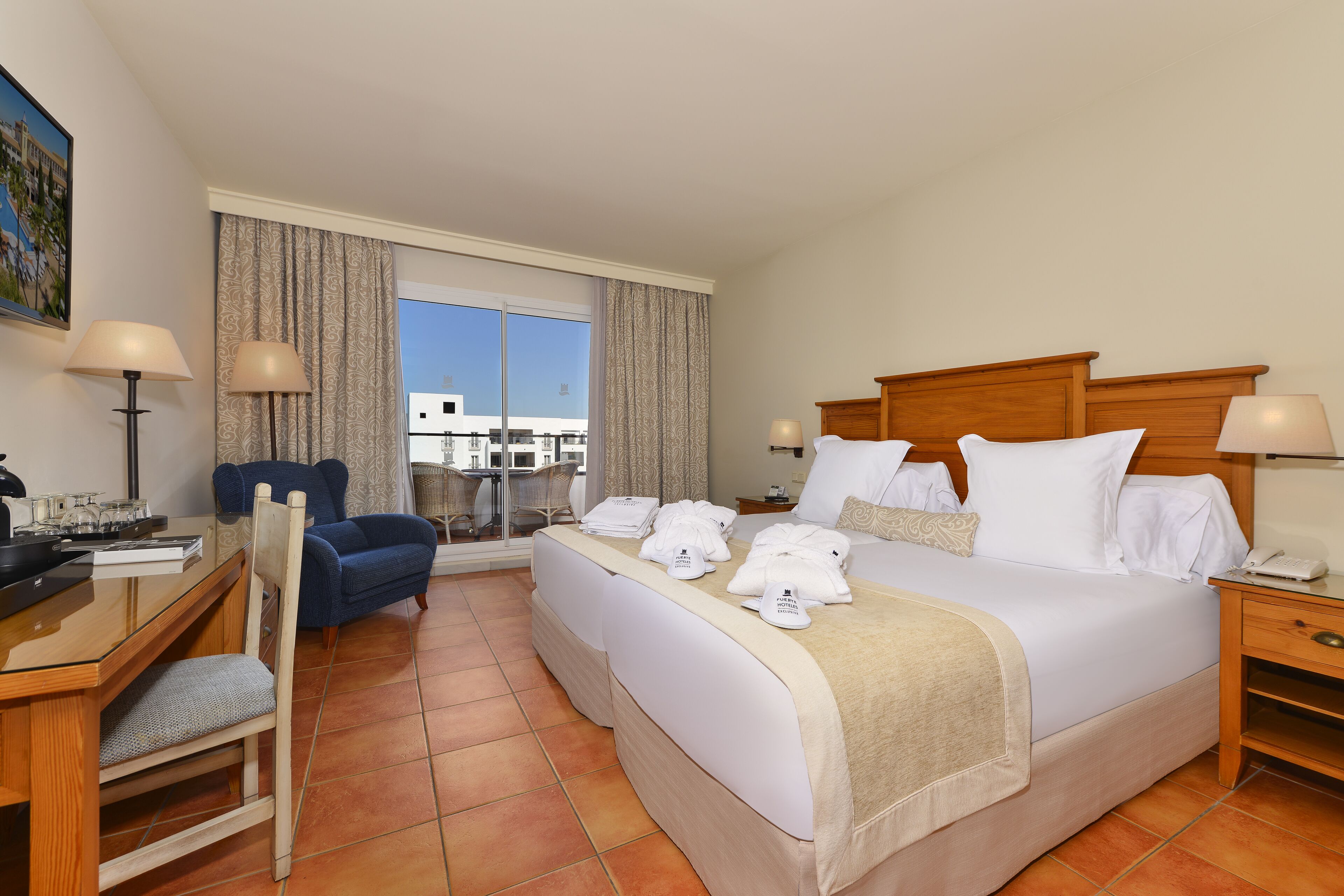 Une chambre d’hôtel avec un lit, deux chaises, un bureau et une fenêtre avec des rideaux.