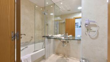 A modern bathroom with a glass-enclosed shower, a glass sink, and a bathtub.