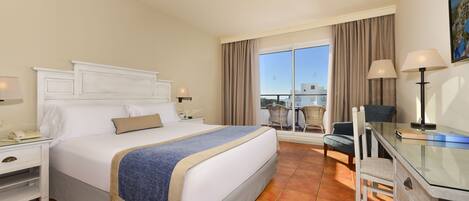 A hotel room with a bed, a desk, a chair, a nightstand, and a view of the outside.
