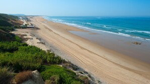 A beach with a long stretch of sand, a few buildings, and a clear blue sky. - Hotel Fuerte Conil-Resort (Conil de la Frontera)